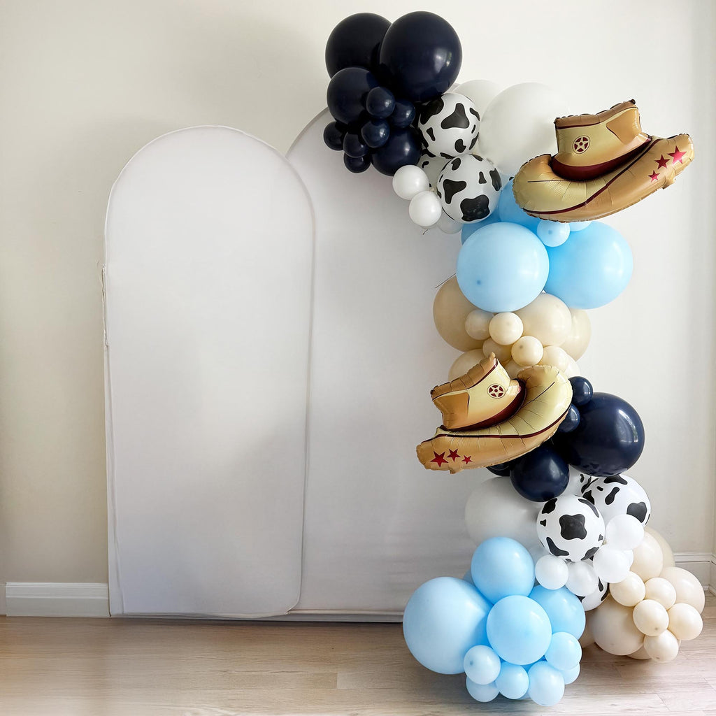 A balloon arrangement featuring various balloons, including some with cow-like designs, is displayed against a white wall.