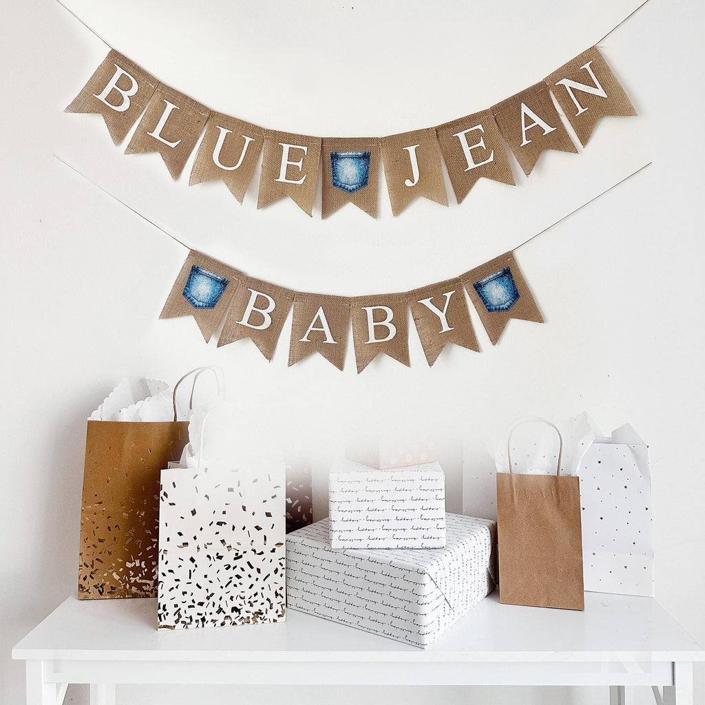 a festive scene with a banner that reads "BLUE JEAN BABY" and various gift bags and boxes arranged on a white table.