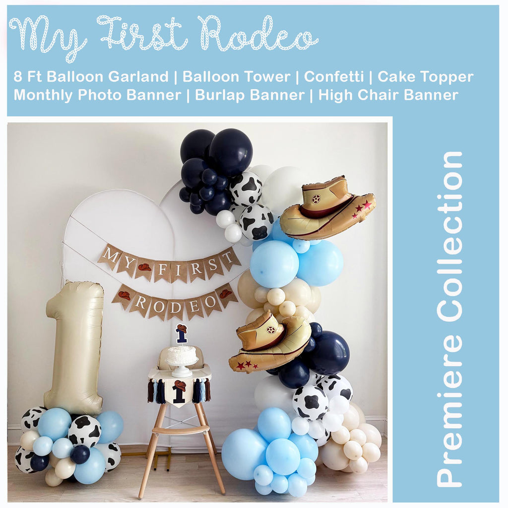 The image is a festive scene set up for a baby's first birthday celebration. It features a balloon tower, a cake topper, and a balloon garland. The balloons are in various colors, including blue, white, and brown. The backdrop is a white wall, and there is a banner that reads "My First Rodeo". The overall scene is decorated with a cowboy theme, and the image is described as a "Premiere Collection".
