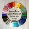 A circular arrangement of colorful tassel strings in various shades of pink, orange, yellow, green, blue, and purple, with a text overlay that reads "Custom Tassel Colors Available! See Description for more details."