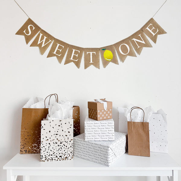 a banner with the word "SWEET ONE" with an image of a lemon between the words, hanging above a table with gifts