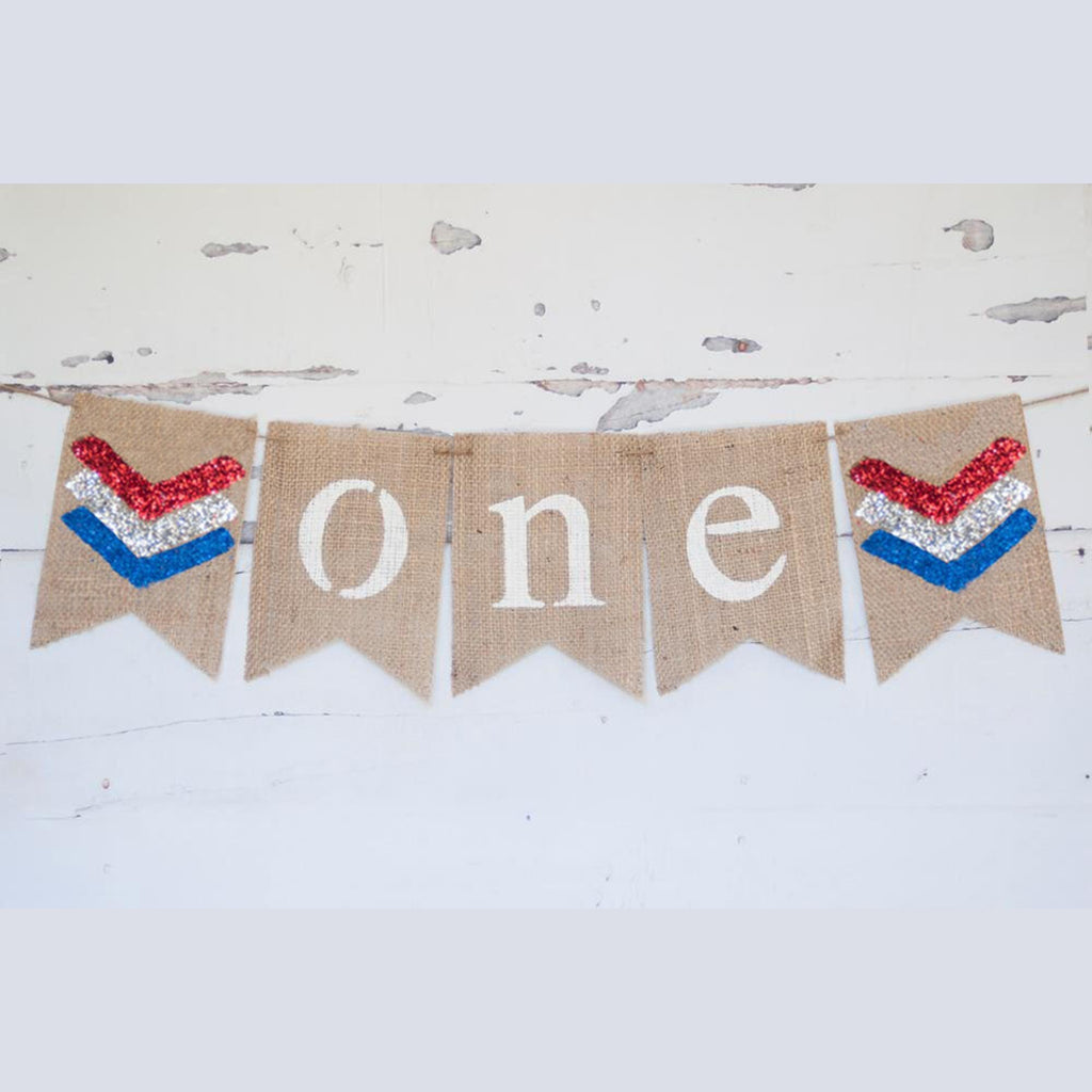 A banner with the word "ONE" written on it, made of burlap and decorated with patriotic colors.