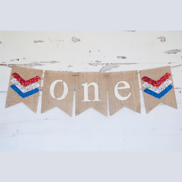A banner with the word "ONE" written on it, made of burlap and decorated with patriotic colors.
