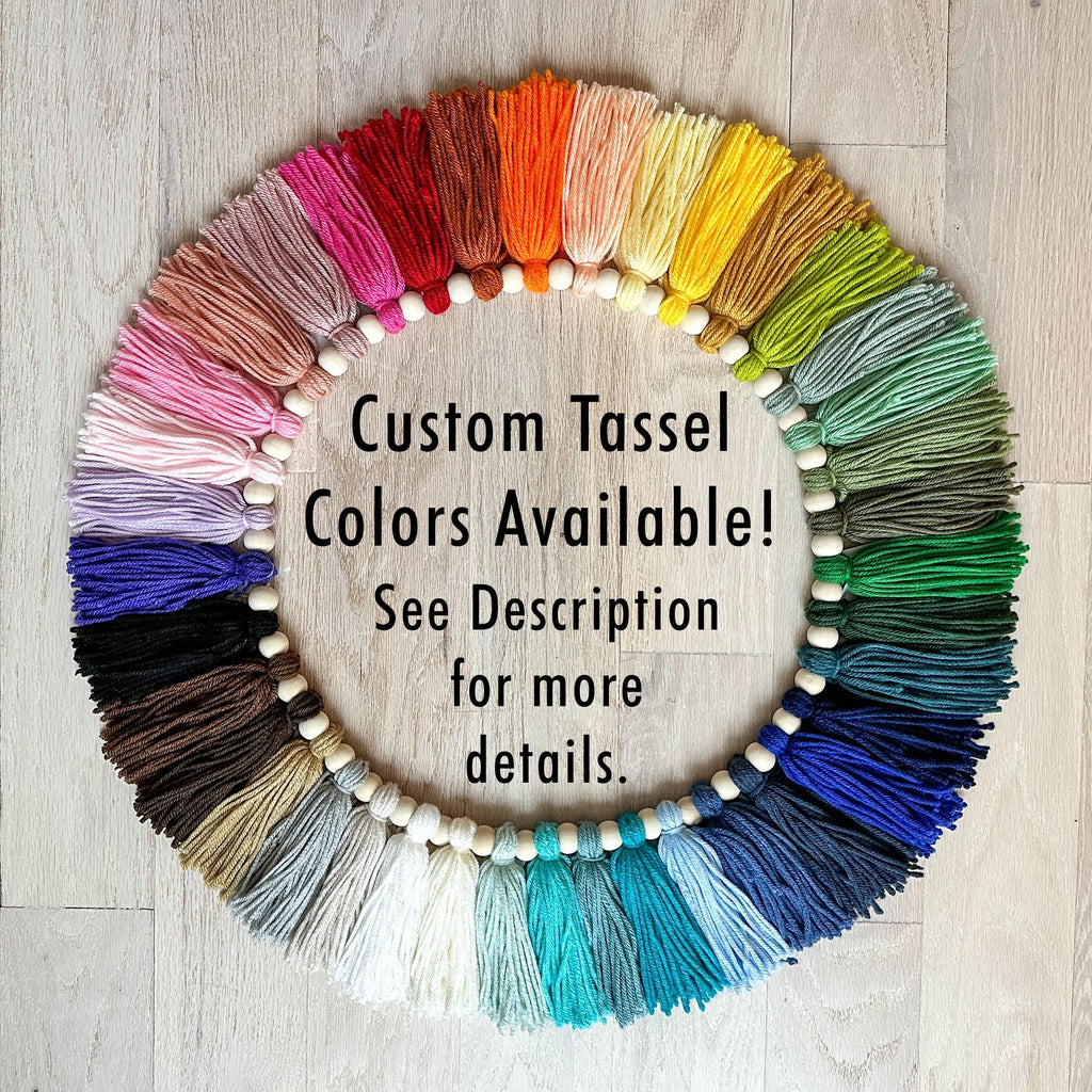 A circular arrangement of colorful tassel strings in various shades of pink, orange, yellow, green, blue, and purple, with a text overlay that reads "Custom Tassel Colors Available! See Description for more details."