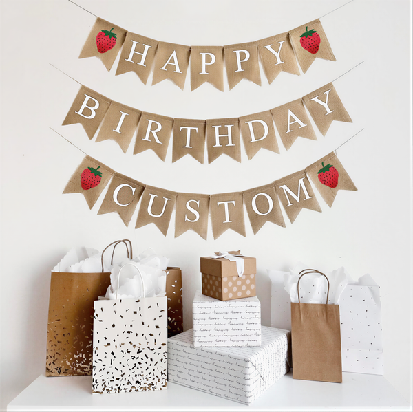 A happy birthday burlap banner strung on two or three strings. The happy is at the top and the birthday below.  Hand painted strawberries are at the beginning and end of the word happy.  The strawberries are painted in red with a green stem and black seeds. This banner has the option to add a third line with a custom name or saying with two additional strawberry image flags.