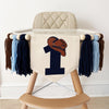 A beige high chair with a white cushion and a banner featuring a cowboy hat and the number 1 printed on it.
