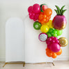 A colorful balloon garland decorated with balloons in the shape of various fruits, including a pineapple, grapes, kiwi, and an orange, against a white background.