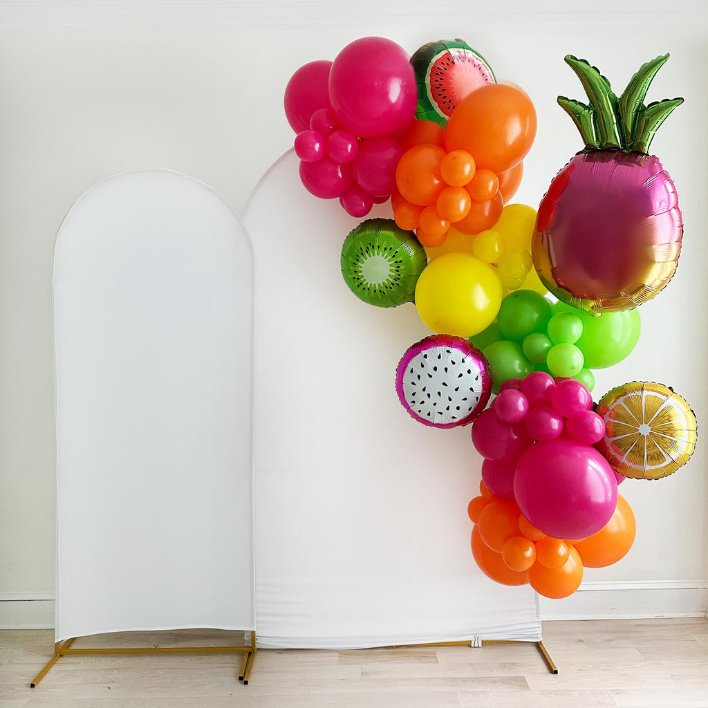 A colorful balloon garland decorated with balloons in the shape of various fruits, including a pineapple, grapes, kiwi, and an orange, against a white background.