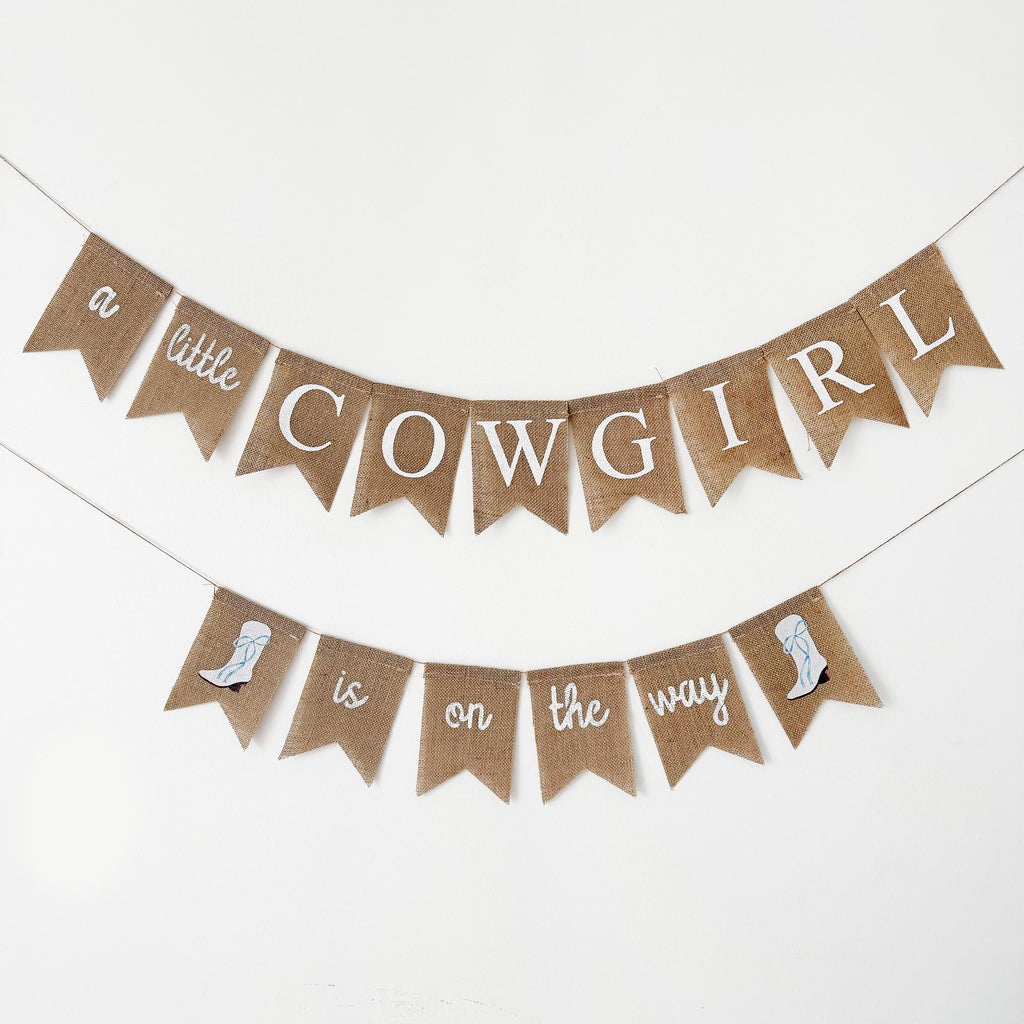 A banner with the text "a little cowgirl is on the way" hanging on a white background.