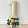 A large gold balloon in the shape of the number one, surrounded by various colored balloons, including green, orange, and white, creating a festive and celebratory display.