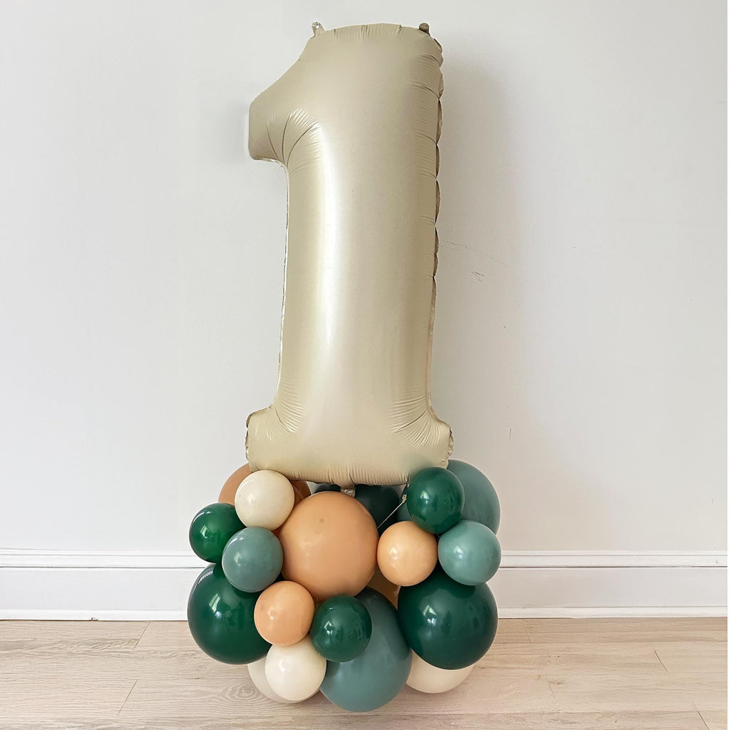 A large gold balloon in the shape of the number one, surrounded by various colored balloons, including green, orange, and white, creating a festive and celebratory display.