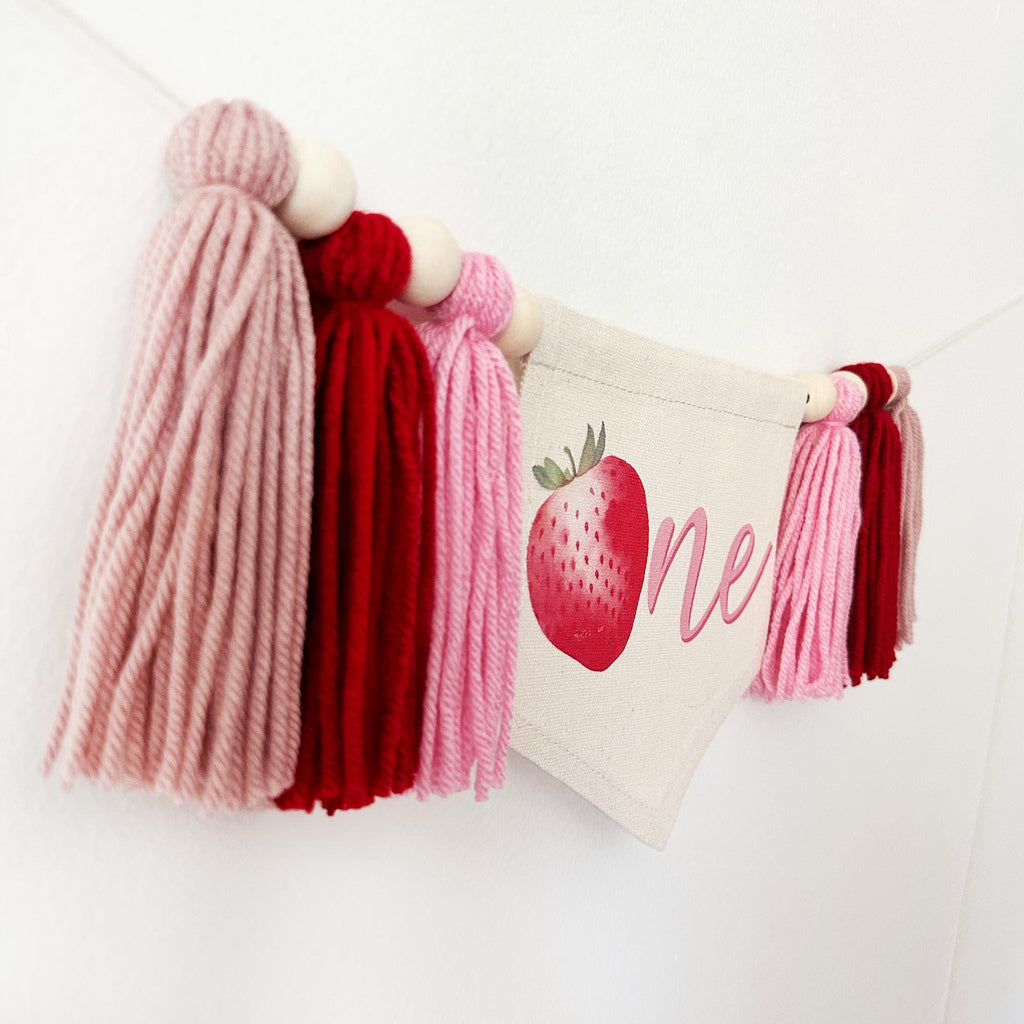 A banner with tassels and a strawberry graphic, hanging on a white wall.