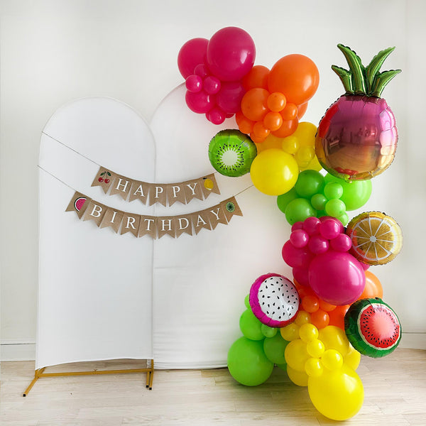A colorful balloon arrangement decorated with fruit shaped balloons with a banner that says "Happy Birthday" in the background.