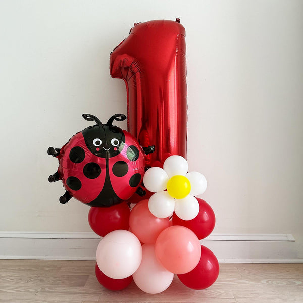 A red balloon in the shape of the number one, with a ladybug design, and a flower-shaped balloon made of pink and white balloons.
