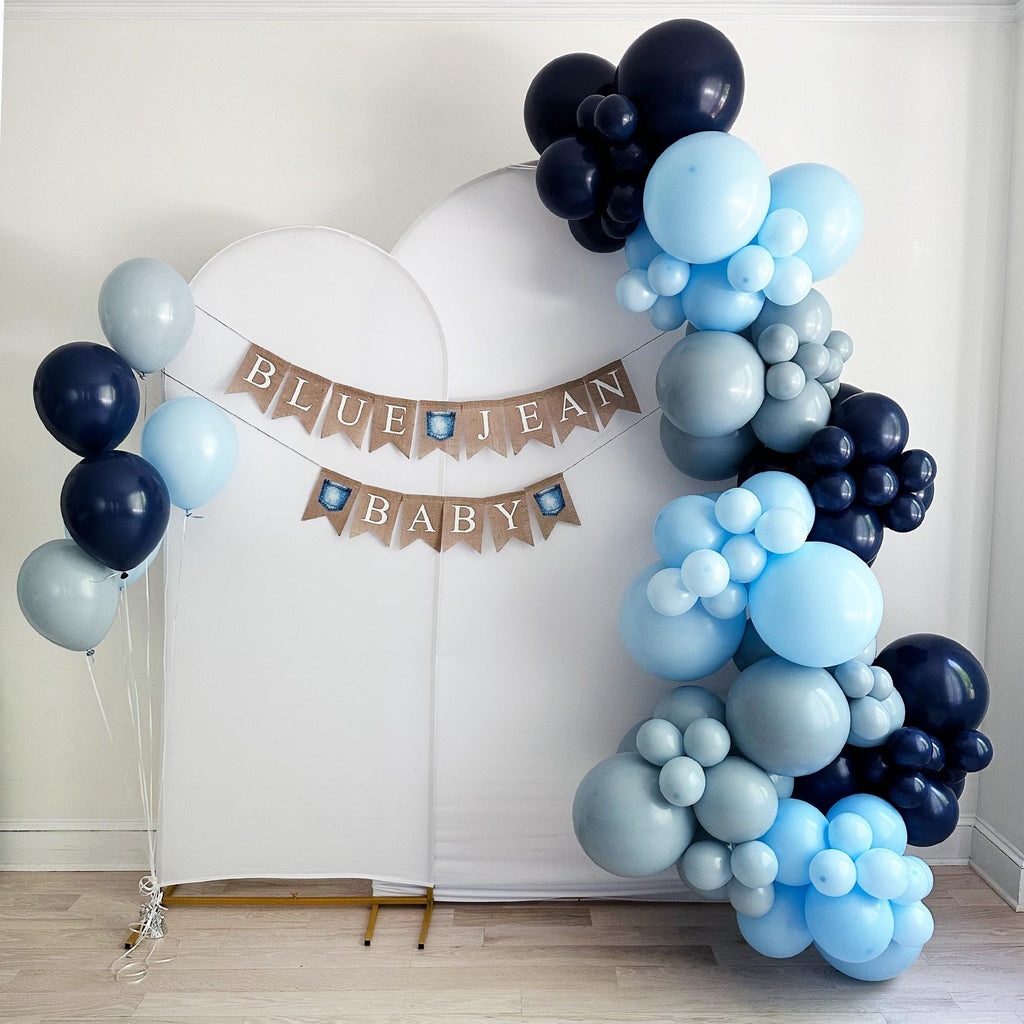 a large balloon arch with the words "Blue Jean Baby" written on it, surrounded by various shades of blue and gray balloons.