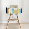 A high chair with a banner displaying the number 1 and a lemon graphic, along with blue and yellow tassels.