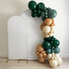 A colorful balloon arrangement in various shades of green, orange, and beige is displayed against a white wall.