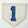 A single blue denim number 1 on a beige canvas flag.