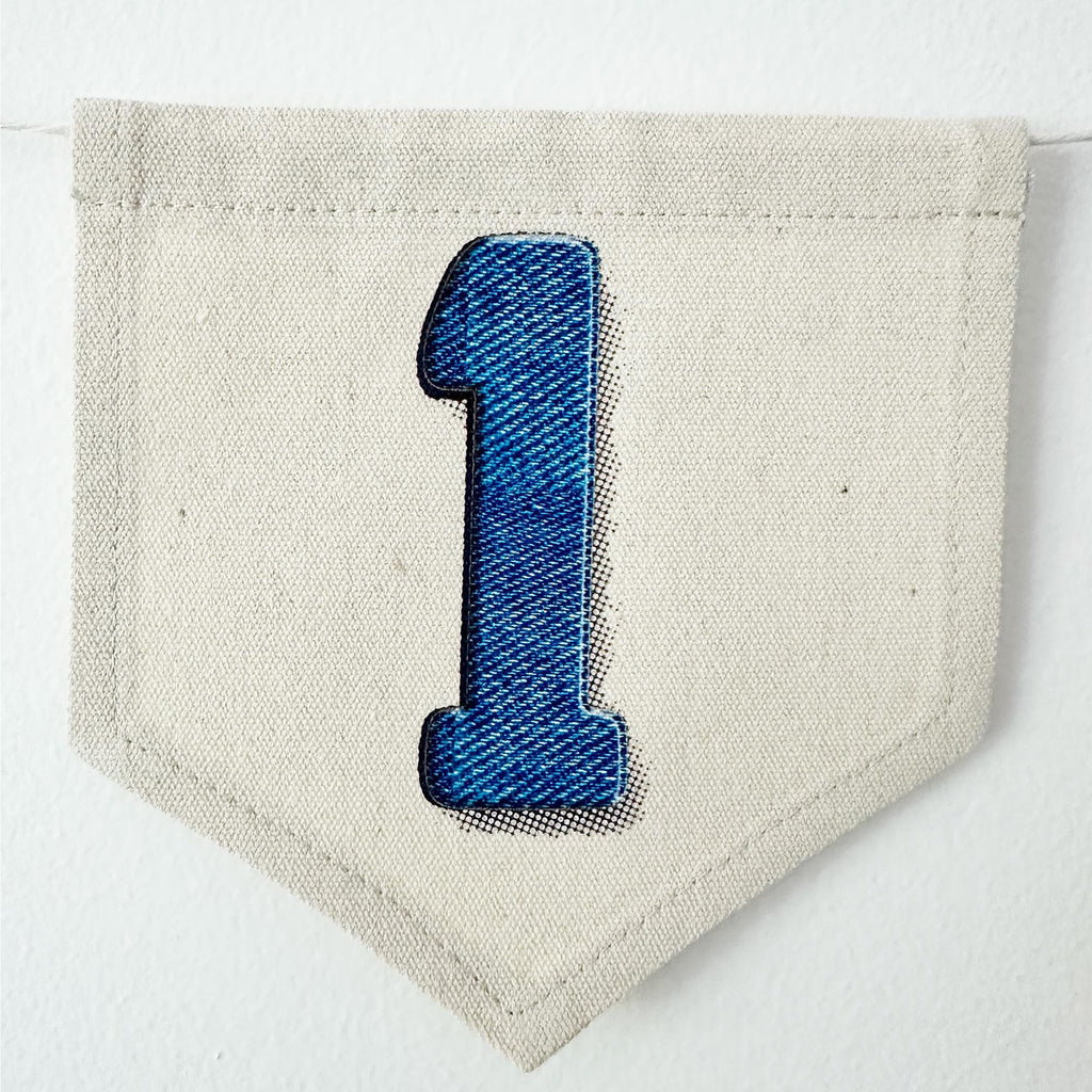 A single blue denim number 1 on a beige canvas flag.