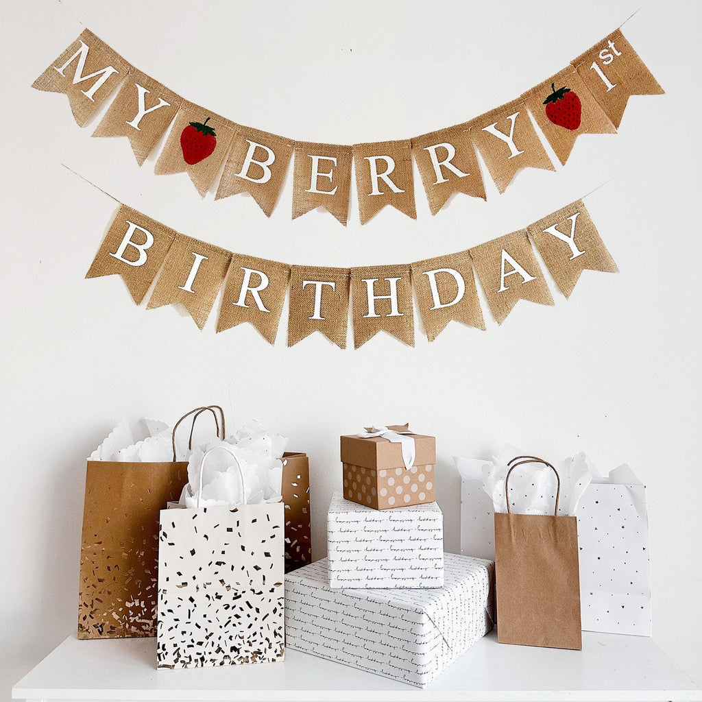 a birthday celebration setup with a banner that reads "My Berry Birthday" and various gift bags and boxes arranged on a white surface.