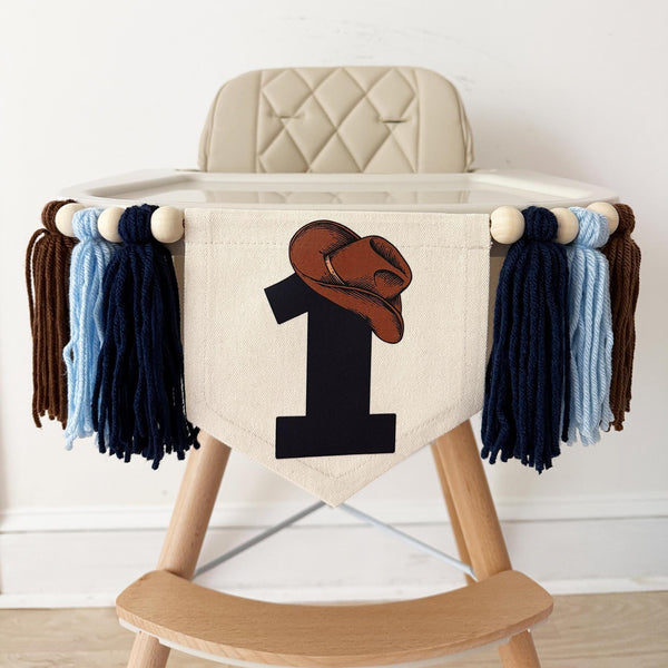 A beige high chair with a banner featuring a cowboy hat and the number 1 on it.