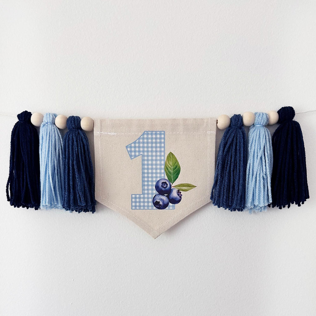 A banner with a blue and white checkered pattern, featuring the number 1 and blueberries, is hanging on a white wall.