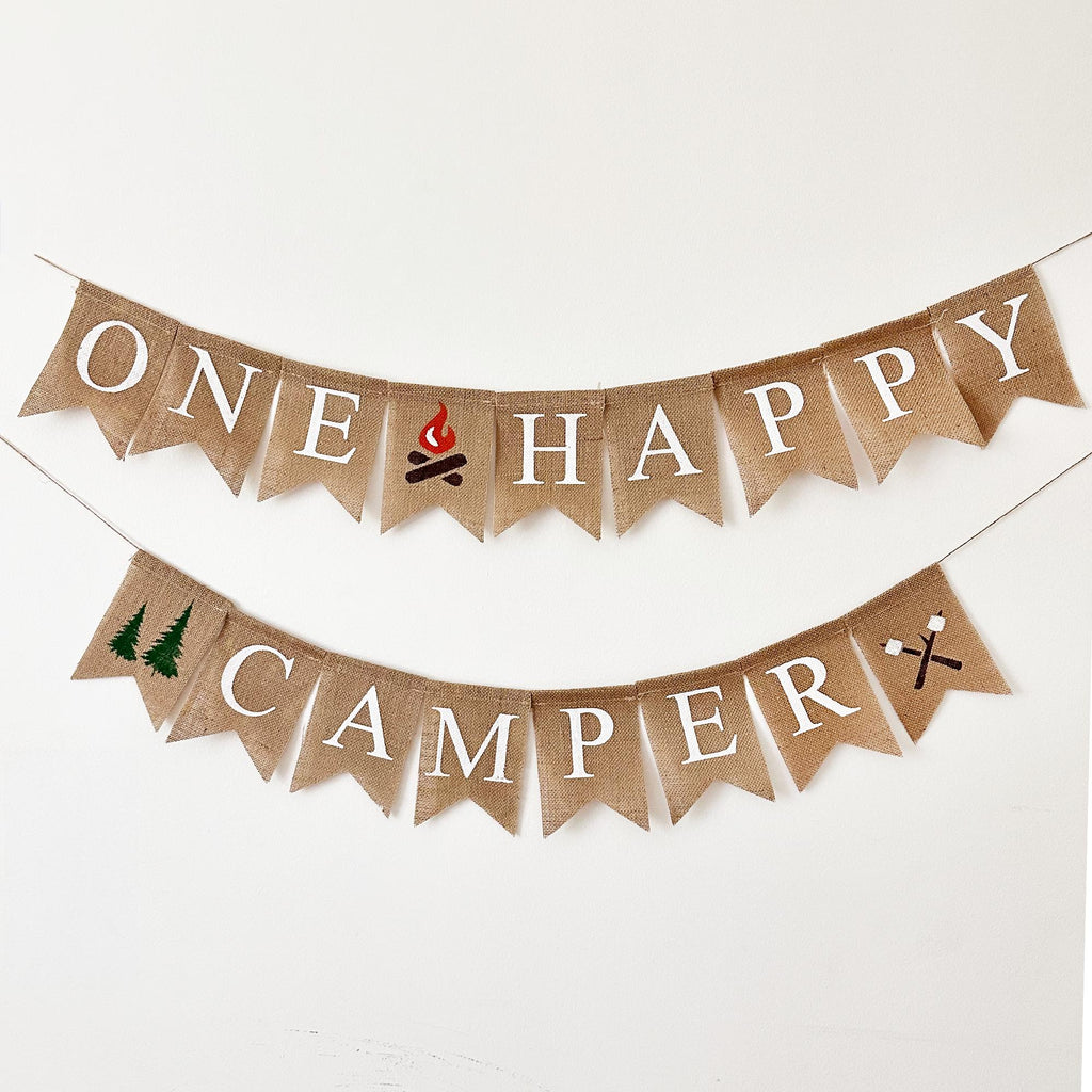 A banner with the words "ONE HAPPY CAMPPER" written on it, along with a small camp fire flag, a tree image banner and a s'mores marshmallow image.