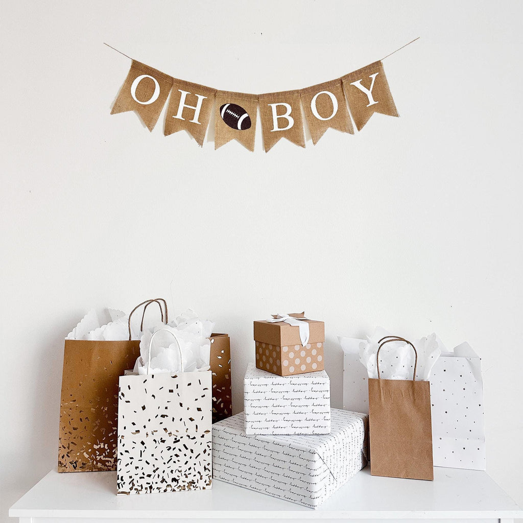 a burlap banner that says "OH BOY" with a football image between the words hanging above a table of gifts.