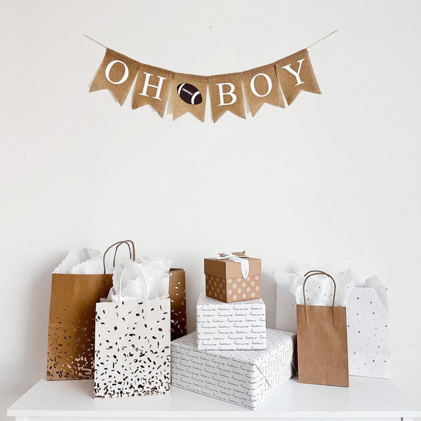 a burlap banner that says "OH BOY" with a football image between the words hanging above a table of gifts.