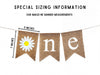 a banner with the word "one" written on it, made of burlap material. The banner is hanging from a string, and there is a measurement scale indicating the banner's size.