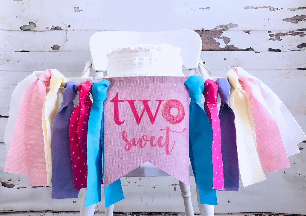 A white high chair decorated with a banner that says "two sweet" and colorful ribbons.