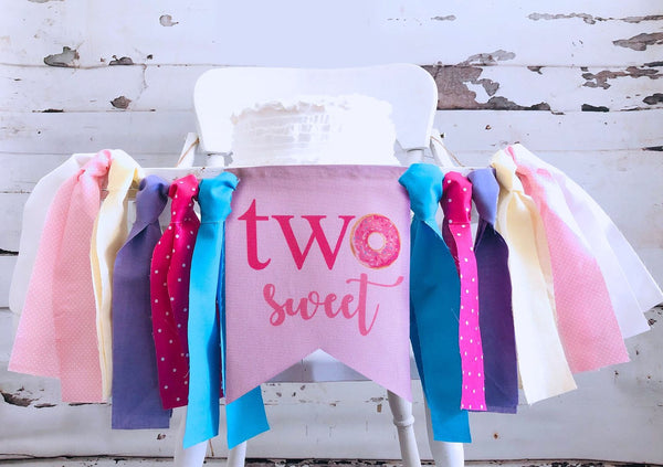 A white high chair decorated with a banner that says "two sweet" and colorful ribbons.