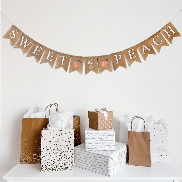 a festive display with a banner that reads "Sweet as Peach" and various gift bags and boxes arranged on a white surface.