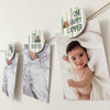 a baby wrapped in a blanket, with a "One Happy Camper" sticker attached to a string above the photo.