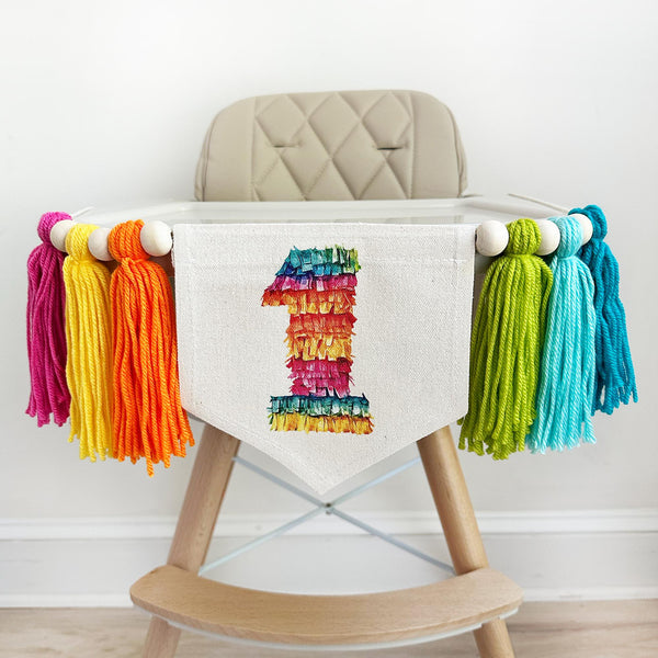 A high chair decorated with colorful tassels and a banner featuring the number 1.