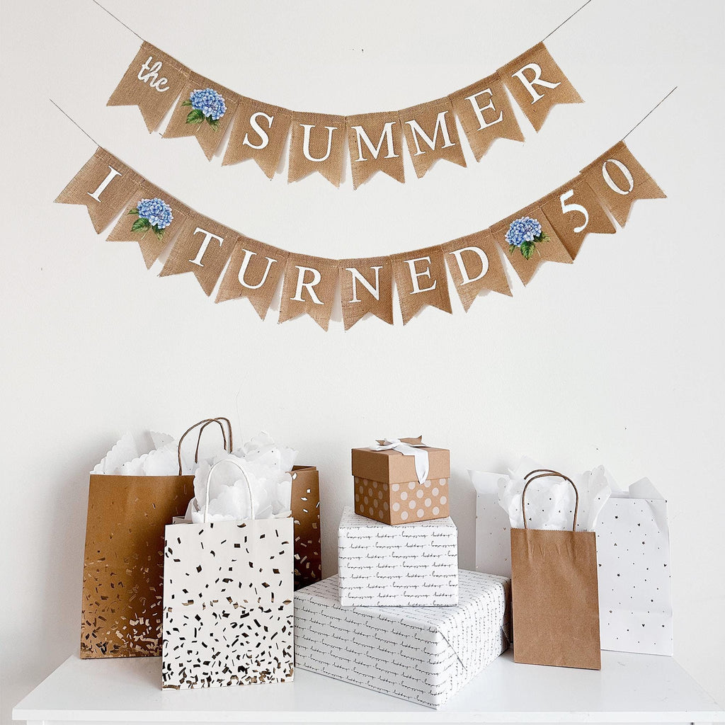 a banner that reads "The summer I turned 50" and a collection of gift bags and boxes on a white surface.