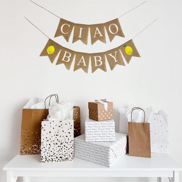 a table with various gift bags and boxes, and a banner that says "Ciao Baby" hanging above it.