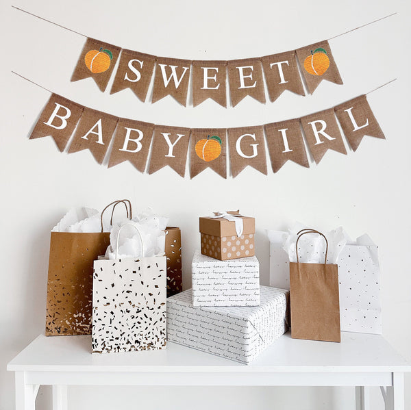 A two tiered burlap banner reading sweet in white text with two peaches on the first line and baby girl with a peach between the words, also in white text.