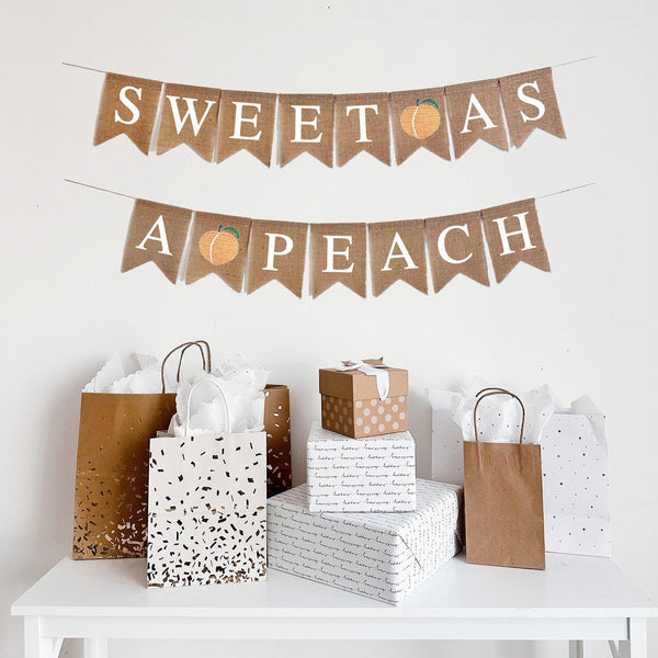 This is a burlap fishtail banner with white letters. It has the words Sweet As on the top string with a peach in between them. It has the words A Peach on the bottom string with a peach in between. Each letter flag measures 4 inches by 6 inches.