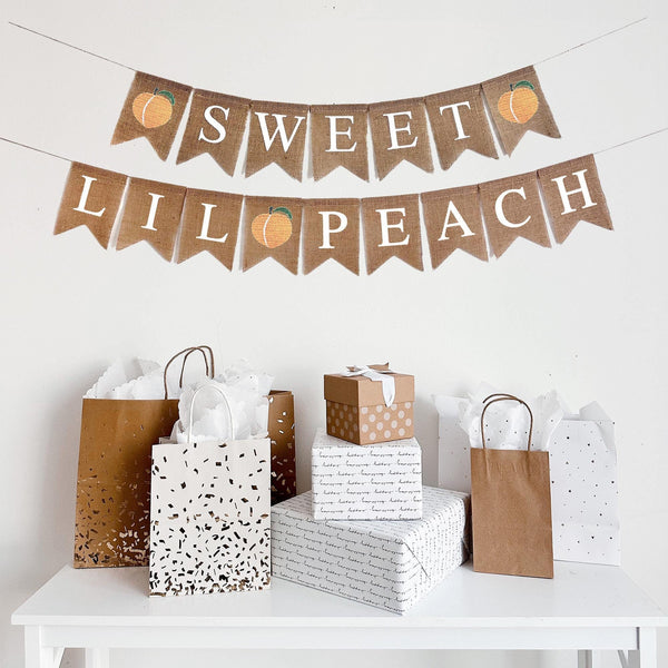 This is a burlap fishtail shaped banner with white letters. The first line has the word Sweet on it in white letters. There is a peach image on either end. The second line has the words Lil Peach with an image of a peach in the middle.