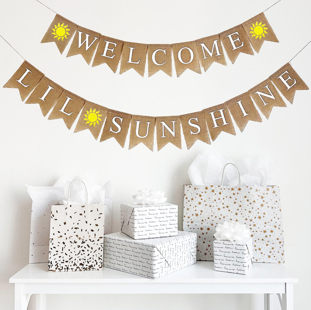 A two tiered burlap banner. The first tier reads Welcome with a hand painted yellow sunshine on either side of the word. The second tier reads lil sunshine with the same yellow sunshine between the words.