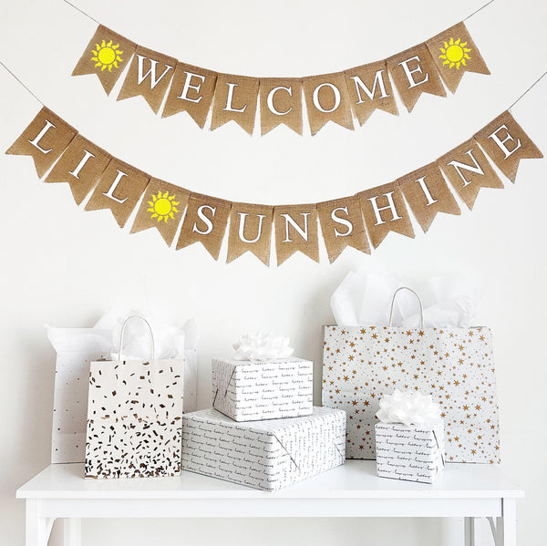 A two tiered burlap banner. The first tier reads Welcome with a hand painted yellow sunshine on either side of the word. The second tier reads lil sunshine with the same yellow sunshine between the words.
