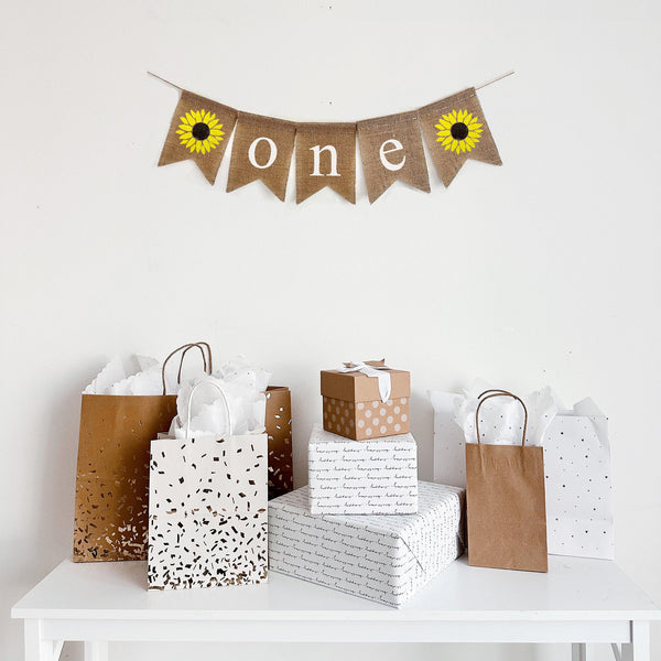 First birthday burlap banner featuring two vibrant sunflowers surrounding the letters o n e written in white paint.