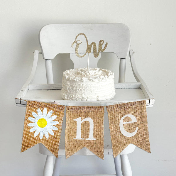 Daisy 1st Birthday high chair banner. This burlap banner has a hand stenciled daisy in place of the O in ONE. Spelling out ONE this banner makes the perfect high chair decor for a retro or boho 1st birthday celebration.