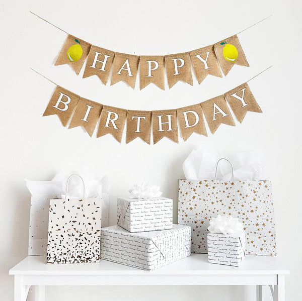 This is a burlap banner with individual fishtail shaped flags. The top line has 7 flags with the word HAPPY in white letters with a lemon on either end of the word. The bottom line has the word BIRTHDAY in white letters.