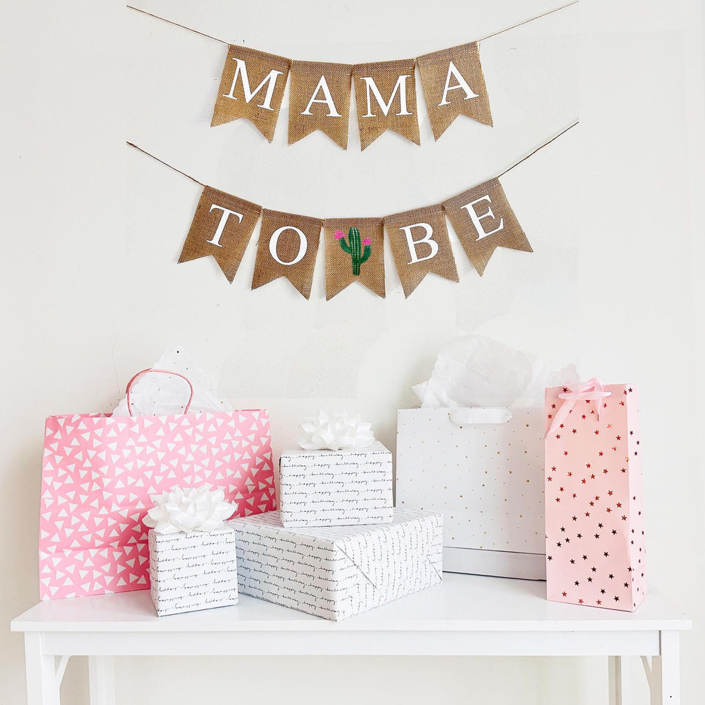 A mama to be burlap banner strung on two strings. The mama is at the top and the to be is below.  Hand painted cacti are in between the words to and be.  The cacti are painted in green with pink flowers.