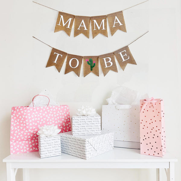 A mama to be burlap banner strung on two strings. The mama is at the top and the to be is below.  Hand painted cacti are in between the words to and be.  The cacti are painted in green with pink flowers.