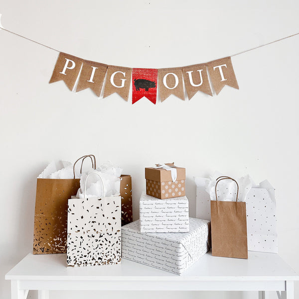 A burlap banner with white text that reads Pig Out with a red burlap banner with a pig silhouette stenciled on the middle. Perfect for a Backyard BBQ Party, Summer birthday or baby shower.
