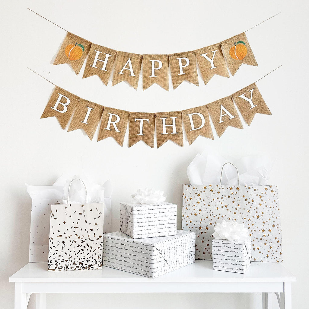 This is a burlap banner made out of 4 inch by 6 inch fishtail flags. It is on two strings. The top string has the word Happy in white letters with an image of a peach on either end. The bottom string has the word Birthday in white letters.