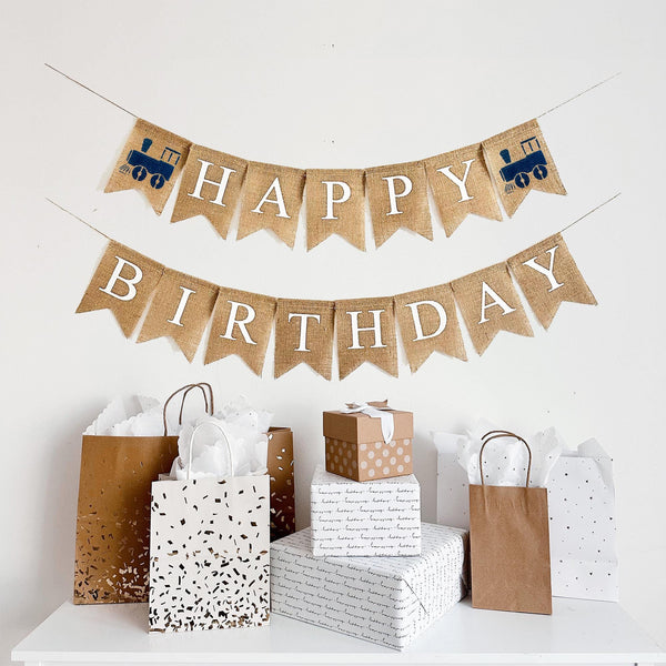 A two tiered burlap banner. The first tier reads happy with navy blue train images on each side. The second line reads birthday.